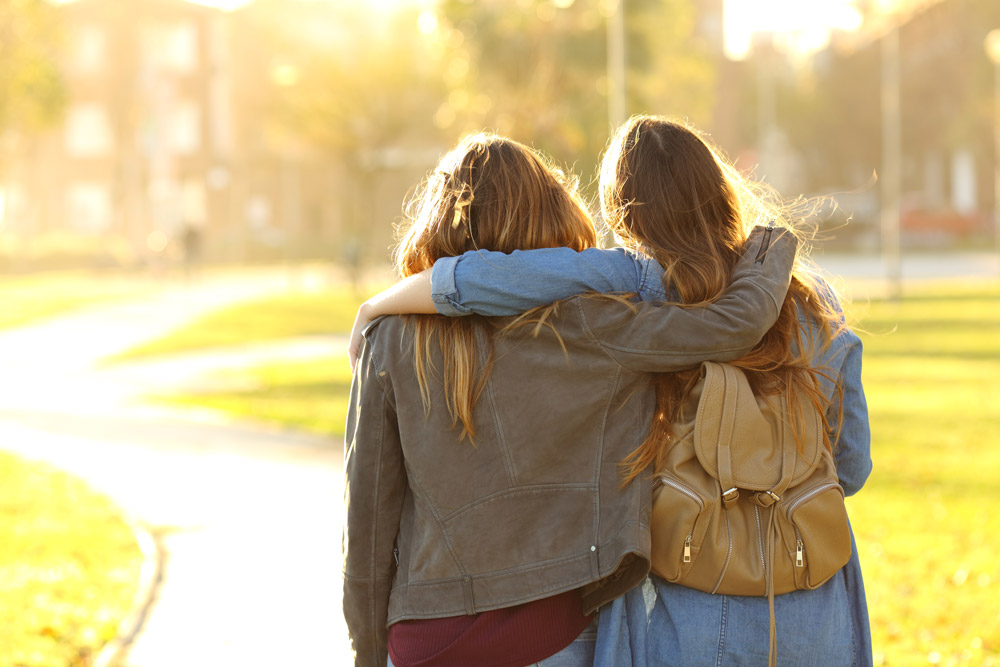 two friends facing away from camera arms on each others shoulders.